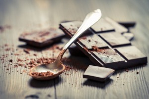Close up of dark chocolate squares and a silver spoon with cocoa powder on them