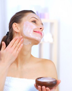 Youthful woman smiling and applying white cream to her face