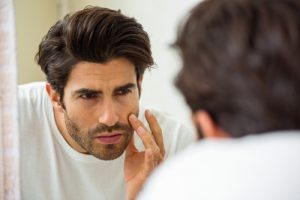 Handsome man looking in mirror touching face